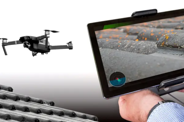 Eine Drohne wird zur Dachinspektion genutzt, gesteuert von Händen mit einem Tablet, um mittels Drohnentechnik Inspektionen oder Aufnahmen durchzuführen.