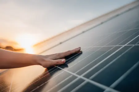 Ein Sonnenuntergang bildet die Kulisse für eine Solaranlage, während eine Hand darüber schwebt und die umweltfreundliche Energiequelle symbolisiert.